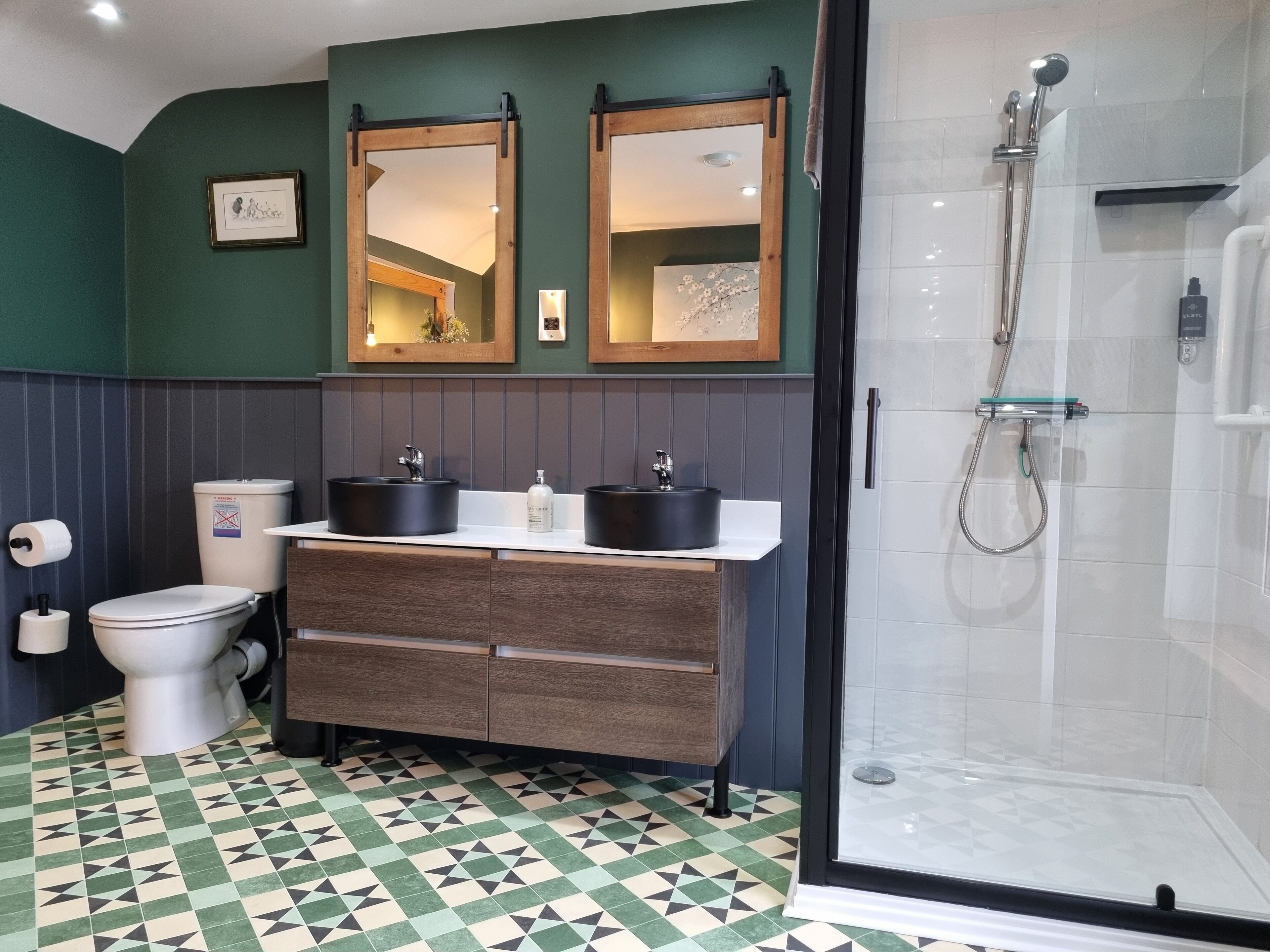 A bathroom with a toilet, two sinks, a shower, and a patterned floor.