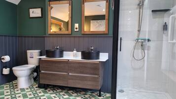 A bathroom with a toilet, two sinks, a shower, and a patterned floor.