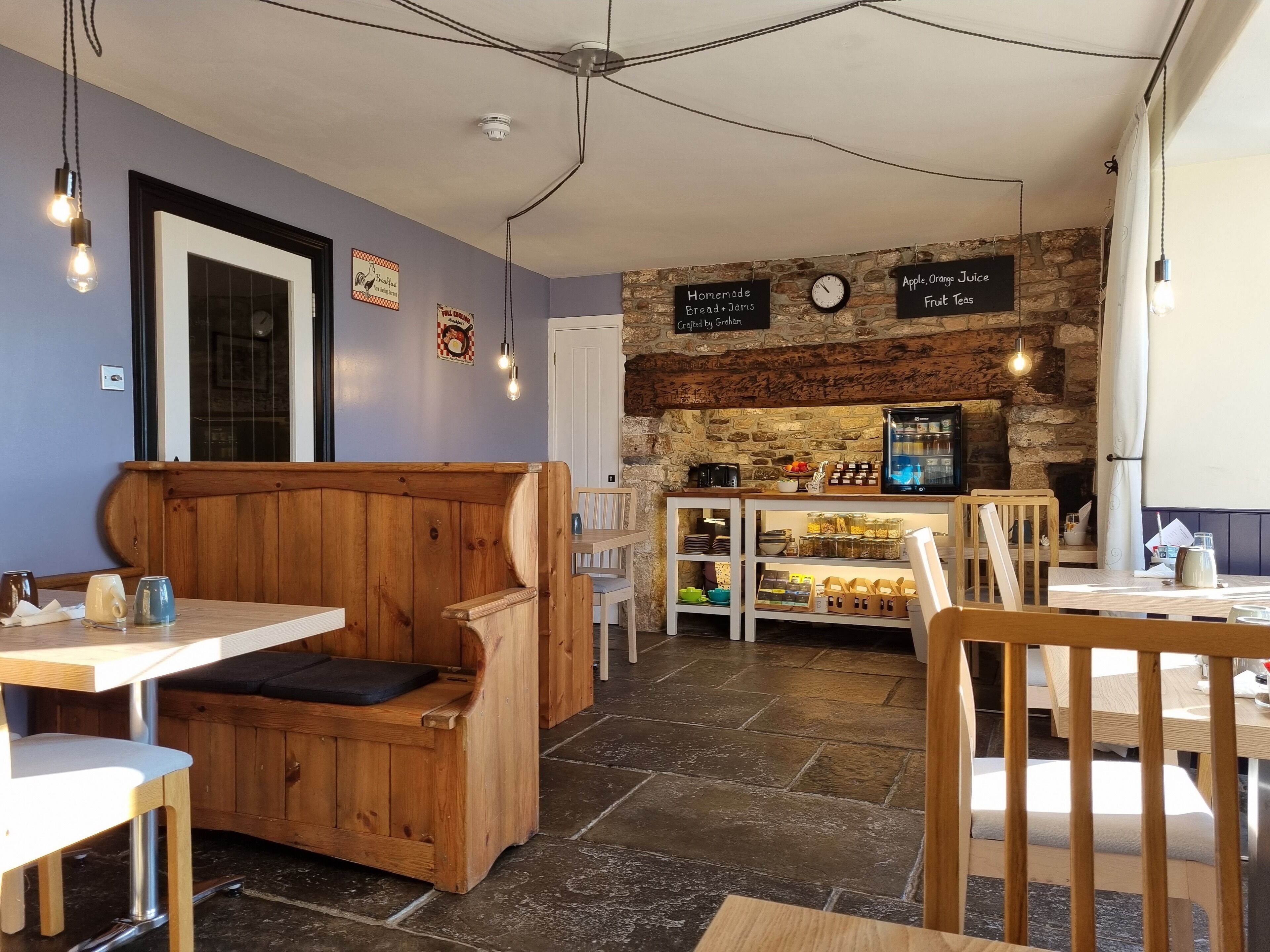 A cozy cafe with wooden furniture, a stone wall, and a menu board displaying homemade bread and jams.