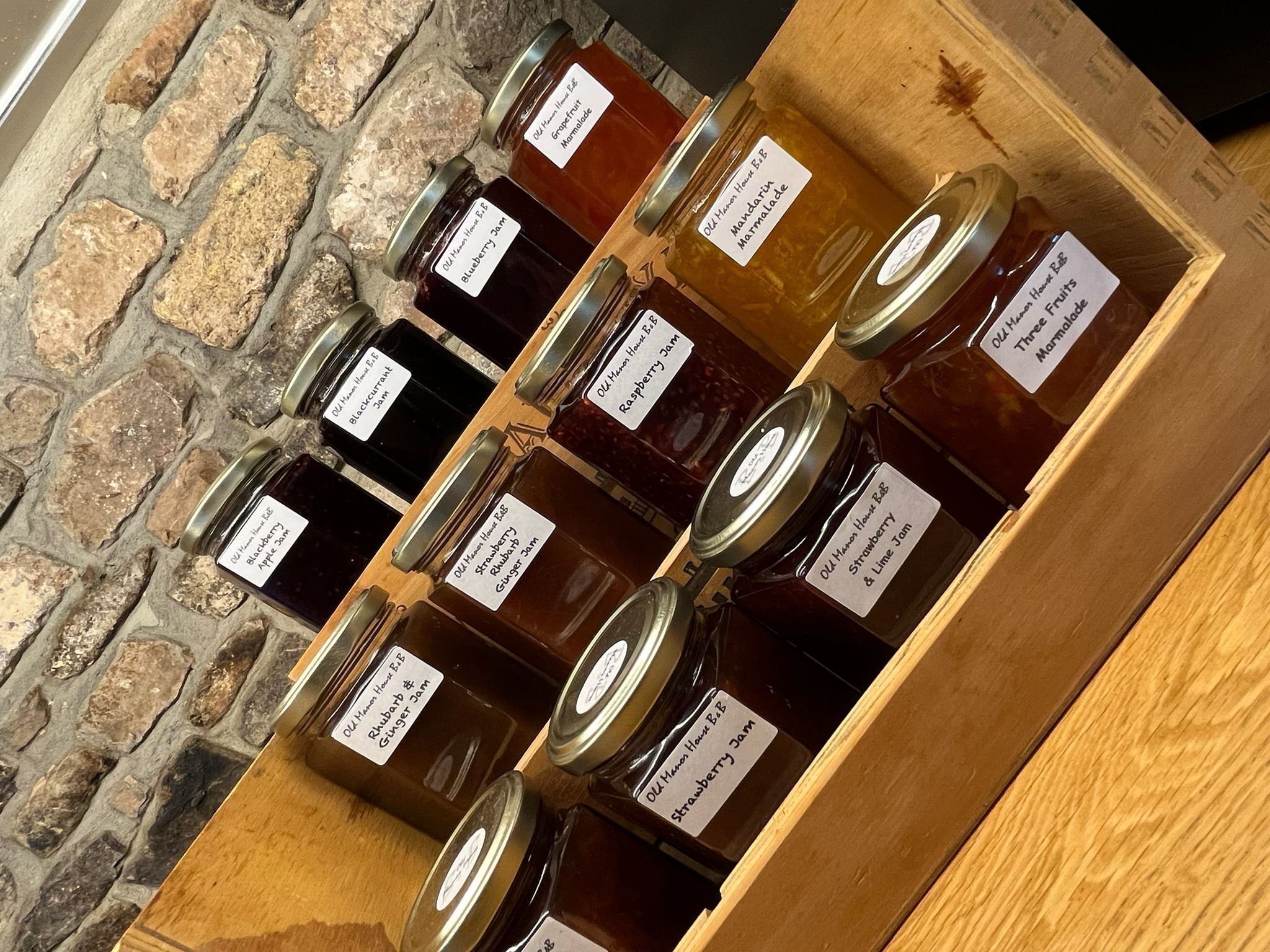 Una vitrina de madera con varios frascos de mermeladas caseras, cada uno etiquetado con el tipo de fruta utilizada.
