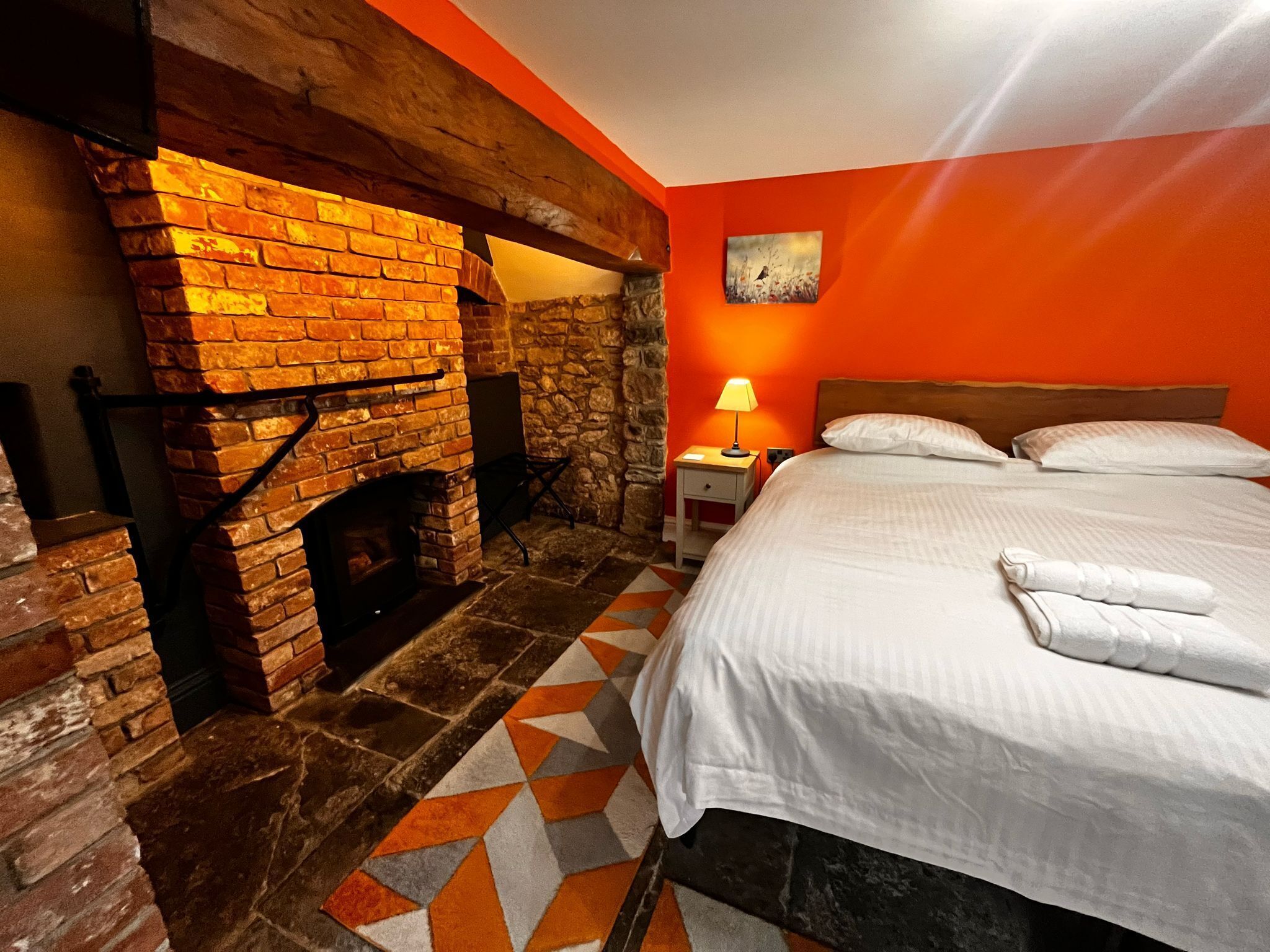 A room with a brick fireplace, a bed with white linens, and a geometric-patterned rug.