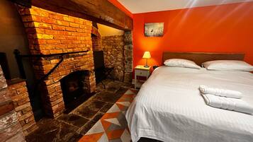 Una habitación con chimenea de ladrillo, cama con ropa blanca y alfombra de diseño geométrico.