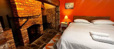 A room with a brick fireplace, a bed with white linens, and a geometric-patterned rug.