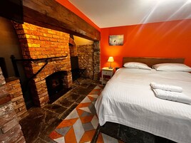 Una habitación con chimenea de ladrillo, cama con ropa blanca y alfombra de diseño geométrico.