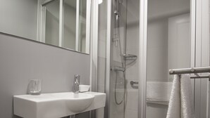Un bany modern amb dutxa de vidre, un lavabo blanc i un mirall a sobre.