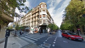Edifici de diverses plantes amb entrada al cantó, pas de vianants i un cotxe vermell al carrer.