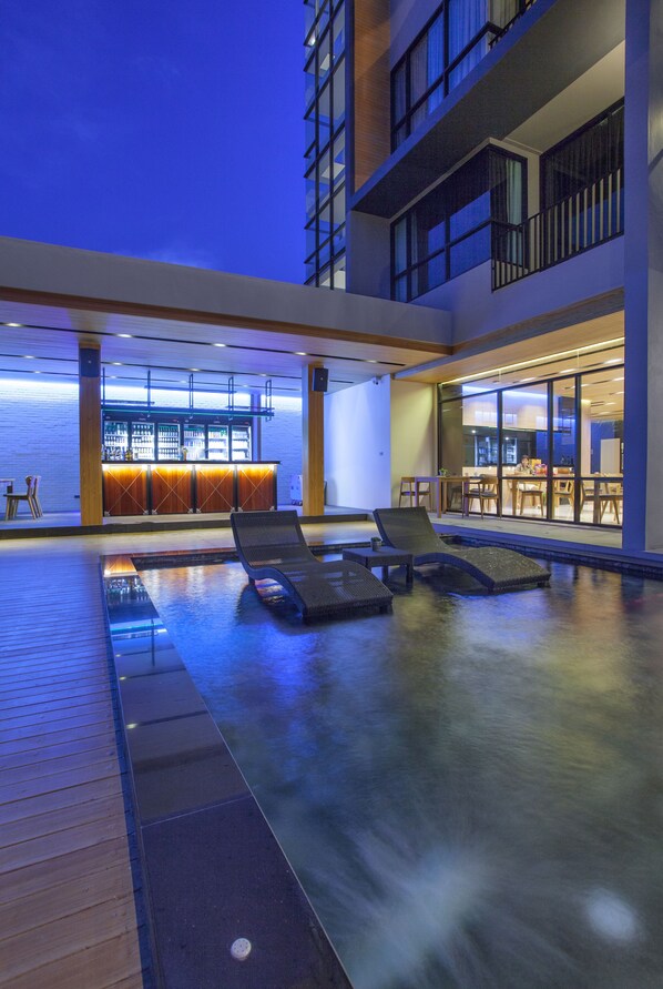 A modern indoor pool area with lounge chairs and a bar.