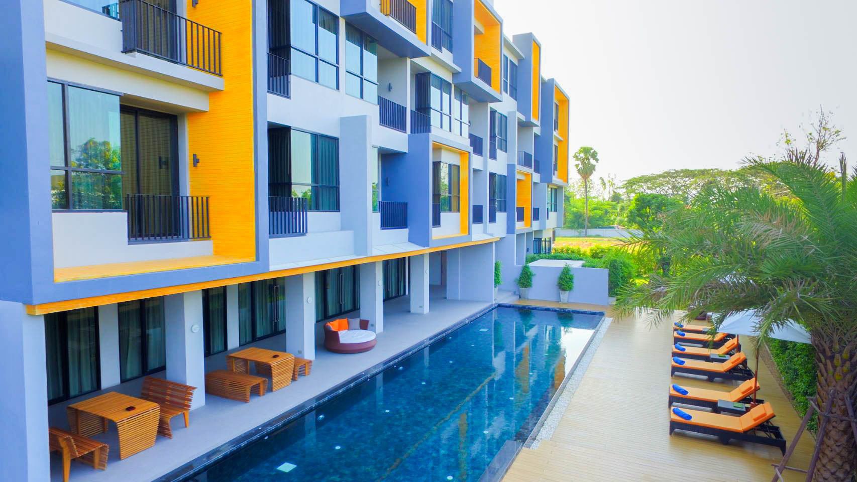A modern hotel with a swimming pool, outdoor seating, and a well-maintained garden.