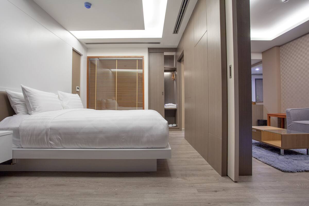 A modern bedroom with a bed, a walk-in closet, and a seating area.