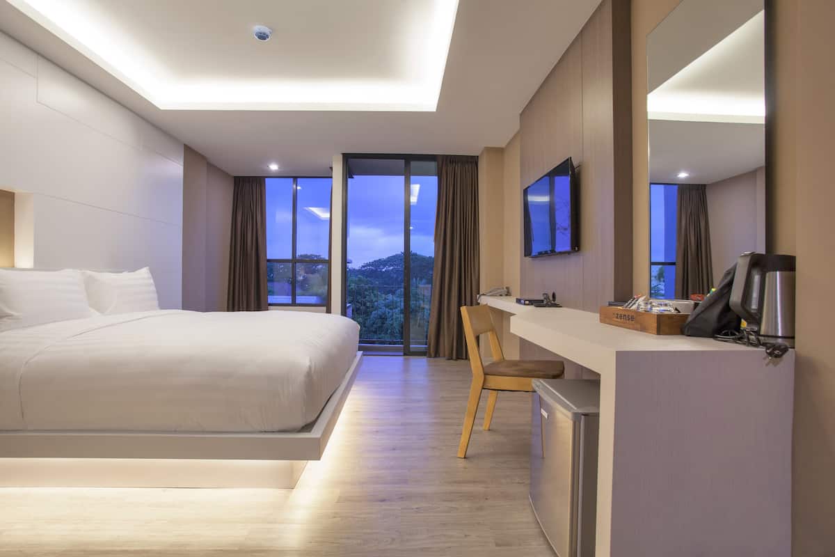 A modern hotel room with a large bed, a desk with a computer, and a view of the outdoors.