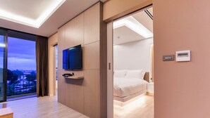 A modern hotel room with a large window, a flat-screen TV, a bed, and a bedside table.