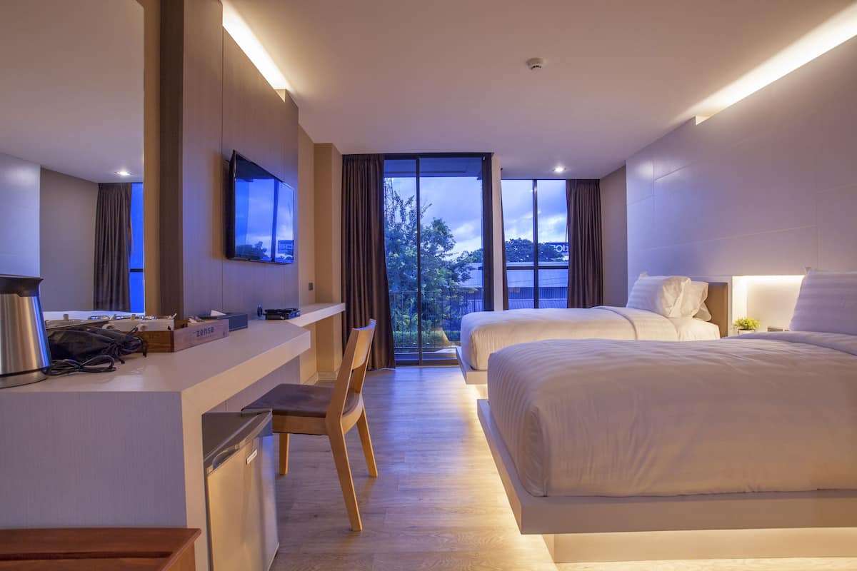A modern hotel room with a desk, two beds, a TV, and a large window with a view.