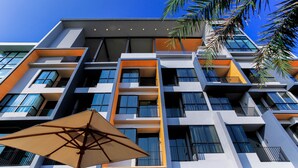 A multi-story building with balconies, large windows, and a palm tree in the foreground.