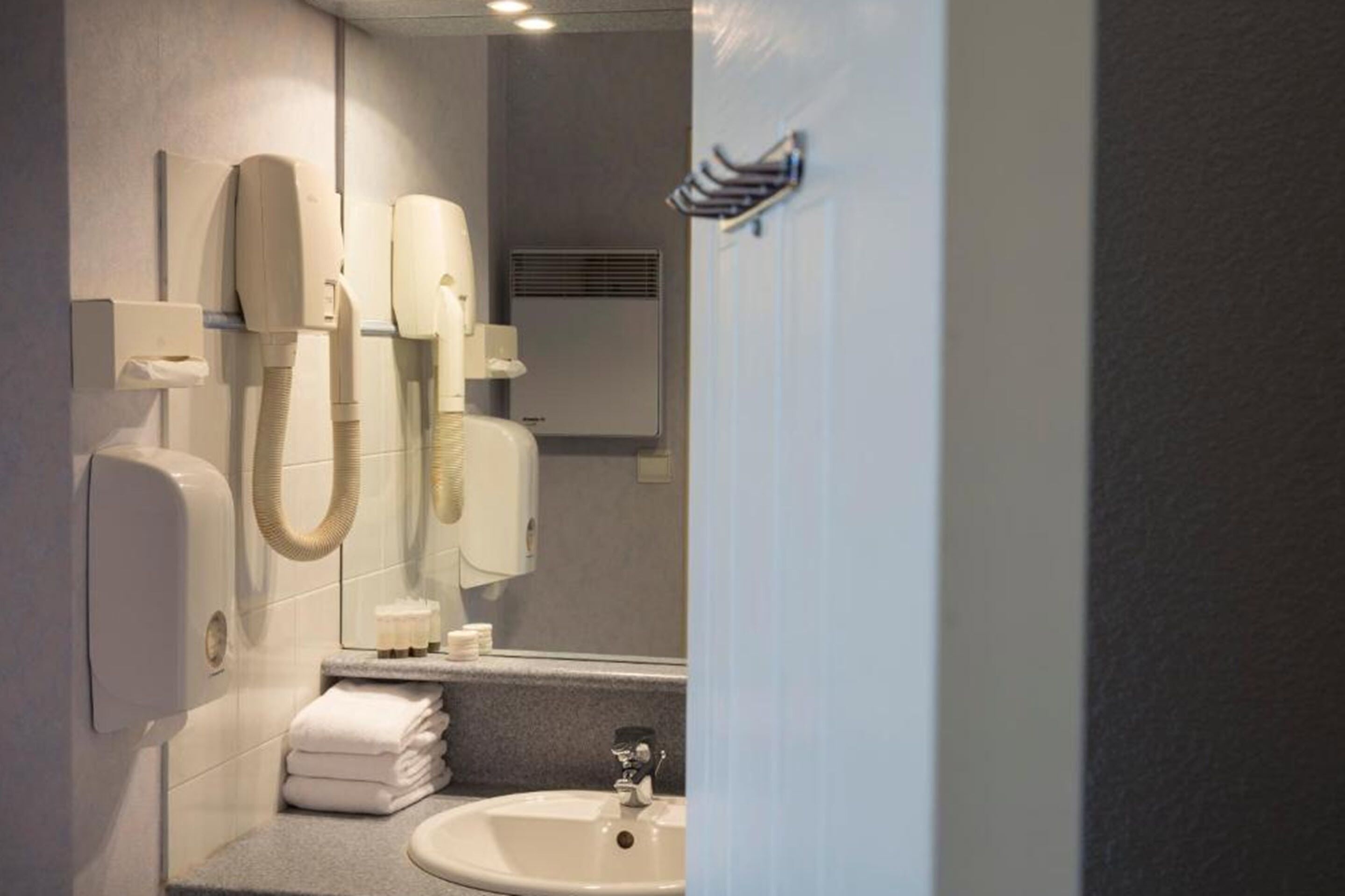 A bathroom with a sink, mirror, and two hair dryers mounted on the wall.