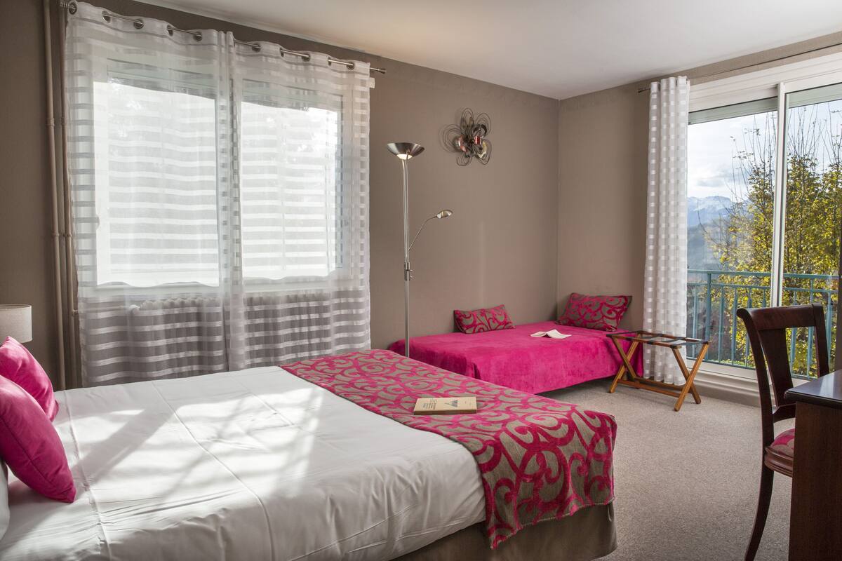 A hotel room with two beds, a balcony with a view, a standing lamp, and a small table.