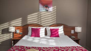 Habitación de hotel con una cama bien hecha, dos almohadas, una lámpara de noche, un teléfono y un cuadro en la pared.