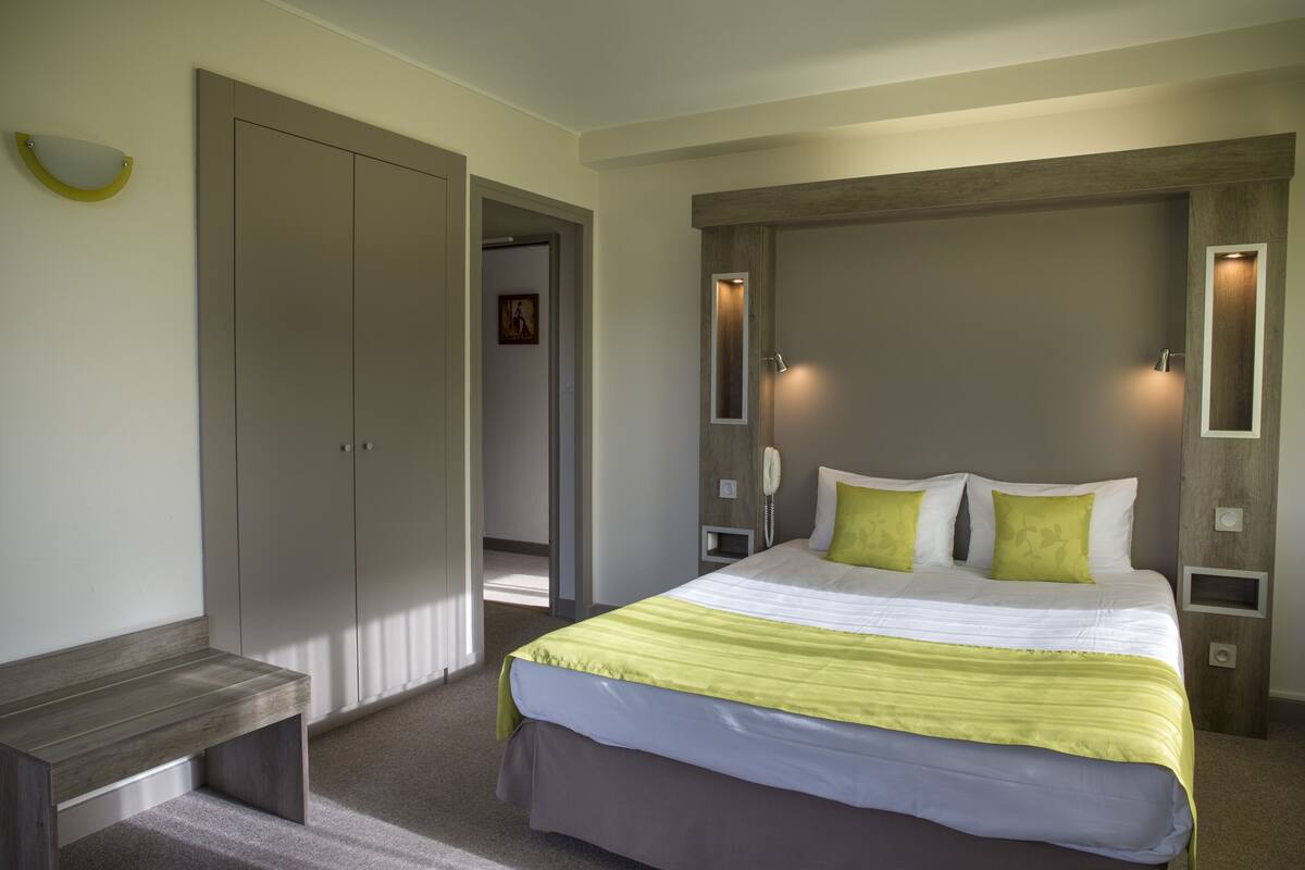 A modern hotel room with a large bed, a bench, a wardrobe, and a wooden accent wall.