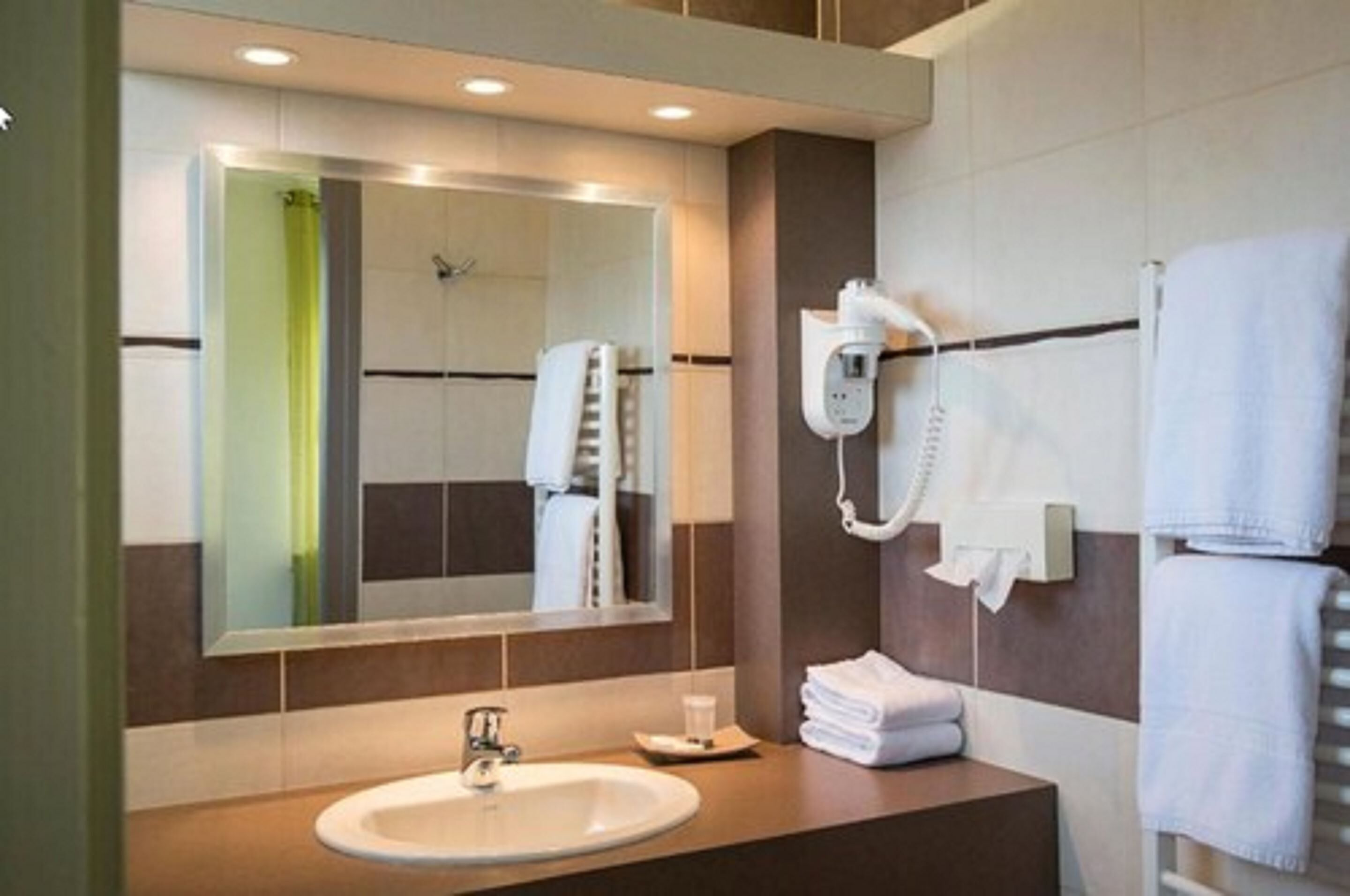 Casa de banho moderna com um espelho grande, uma sanita, um porta-toalhas e um secador de cabelo.