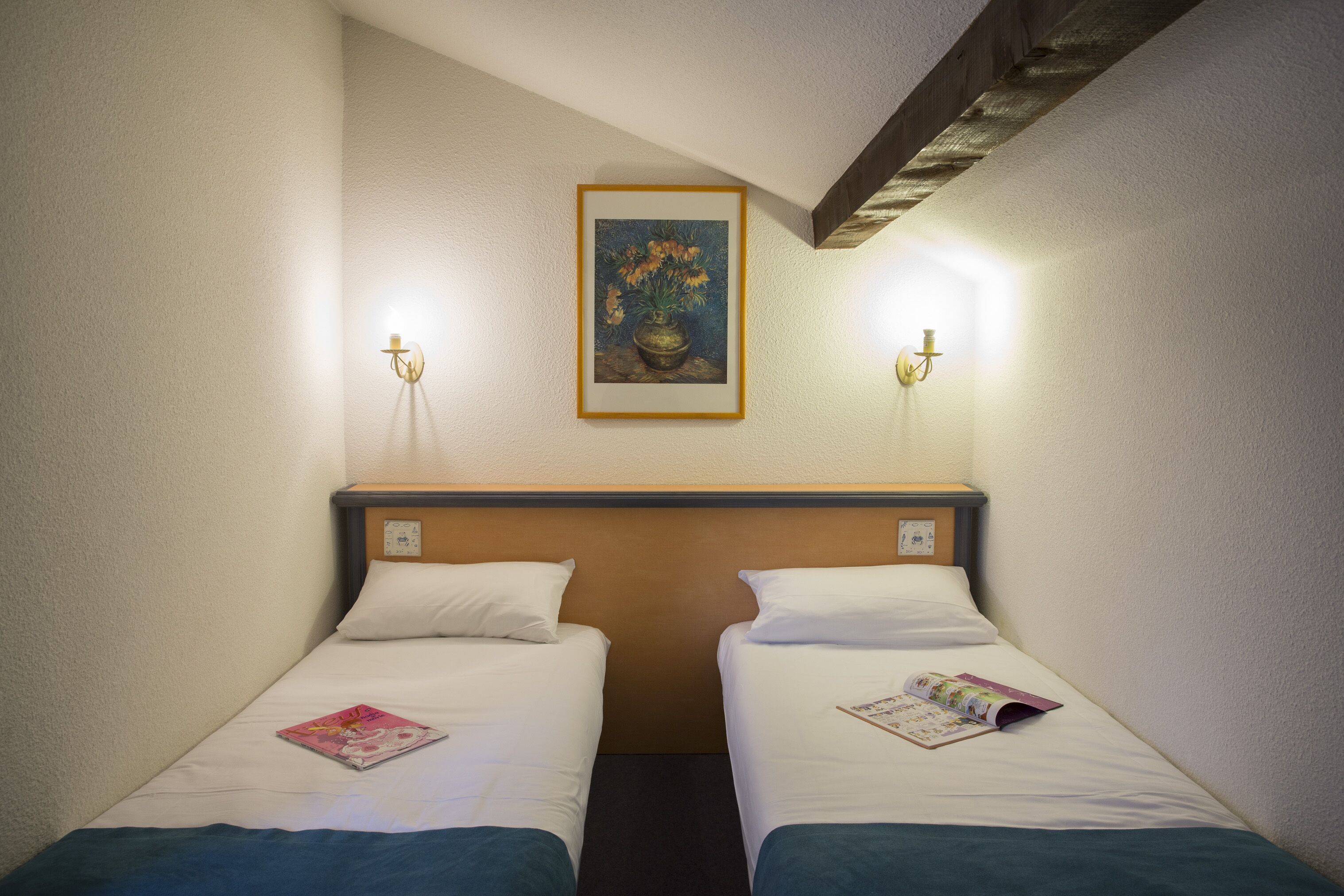 Una habitación de hotel con dos camas, un cuadro en la pared y dos lámparas fijadas a la pared.