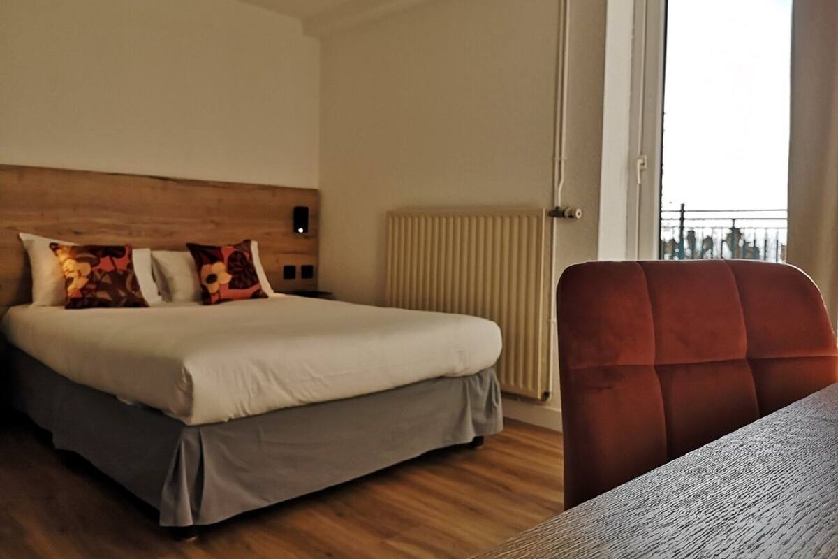 A hotel room with a bed, a chair, a radiator, and a window.