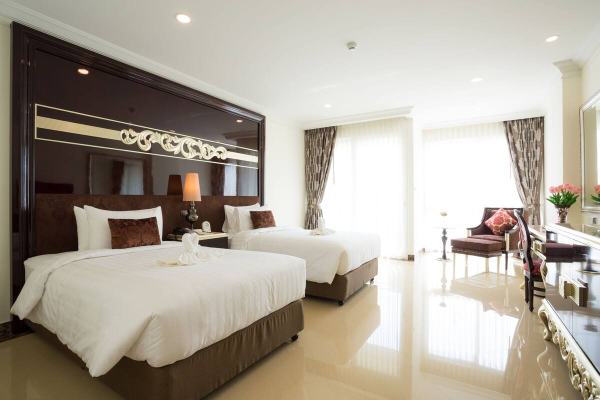 A hotel room with two beds, a sitting area with a chair and a table, and a large mirror.