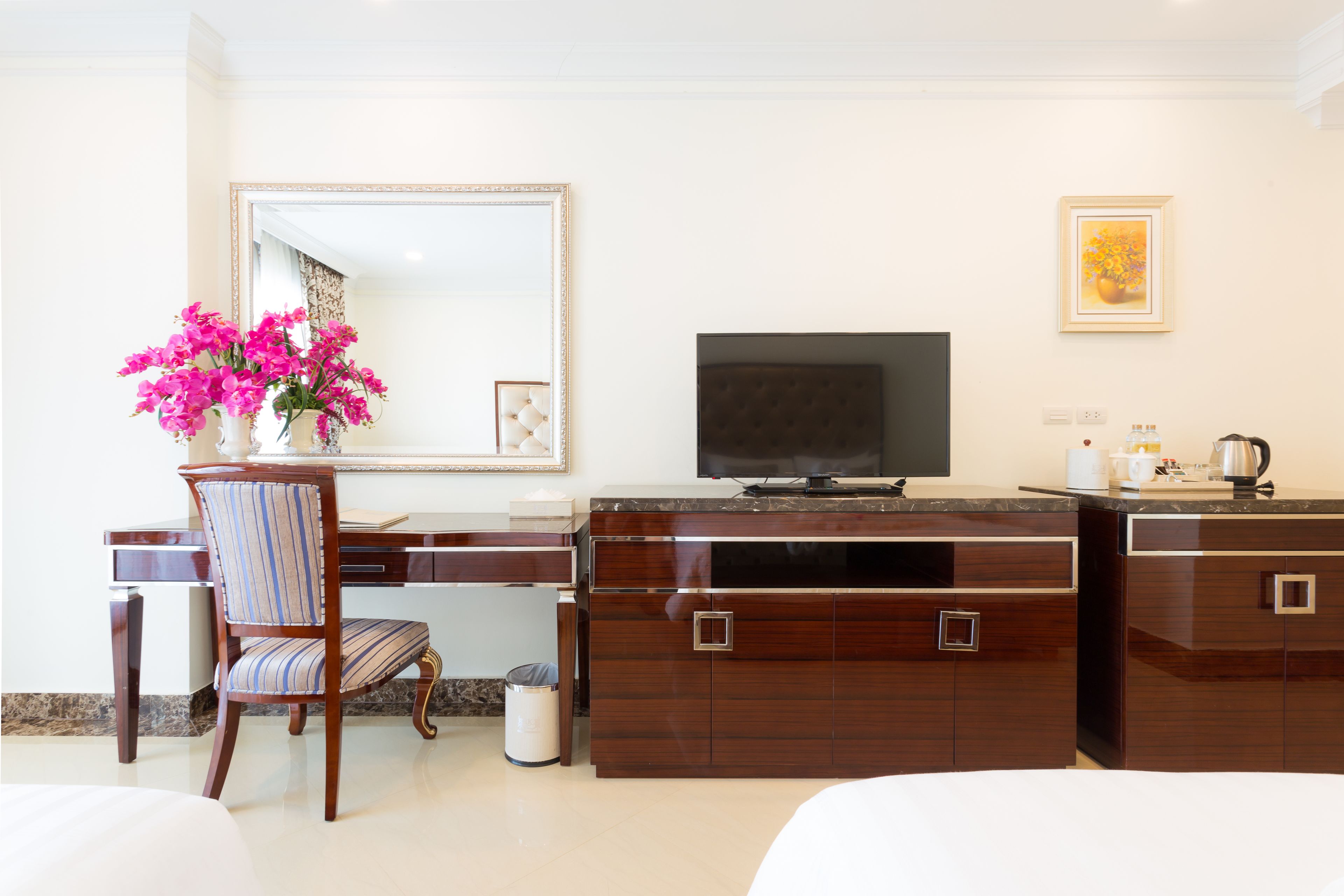 A hotel room with a wooden desk, a television, a mirror, and a bed.