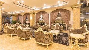 Un hall d’entrée luxueux, agrémenté de meubles richement décorés, d’un sol en marbre et de grandes fenêtres ornées de rideaux.