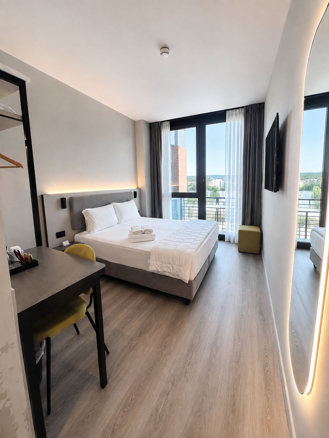 Habitación de hotel con cama, escritorio, silla, televisor y balcón con vistas.