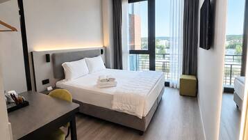 Habitación de hotel con cama, escritorio, silla, televisor y balcón con vistas.