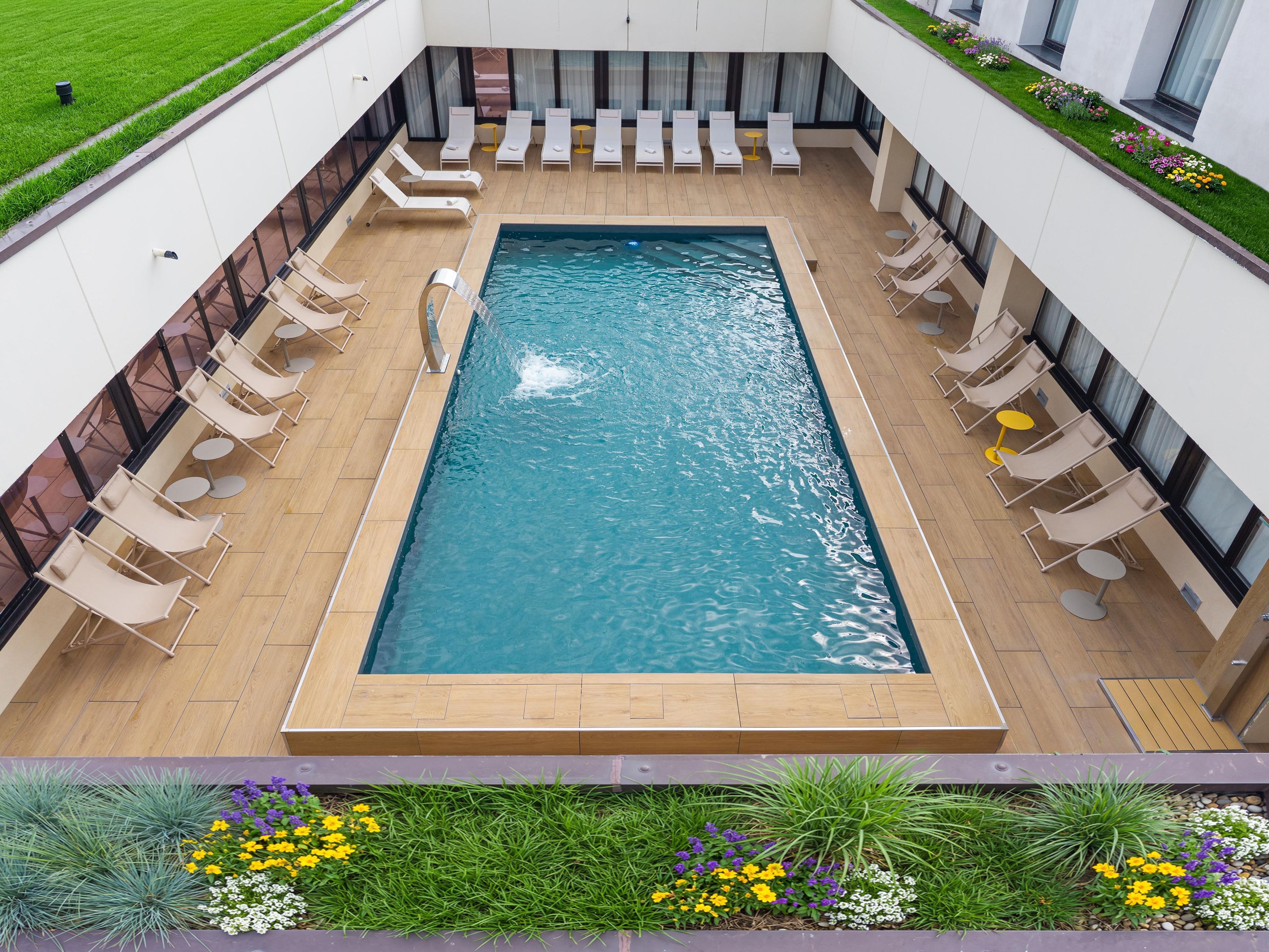 A rectangular swimming pool with a tiled deck, surrounded by lounge chairs and small round tables.