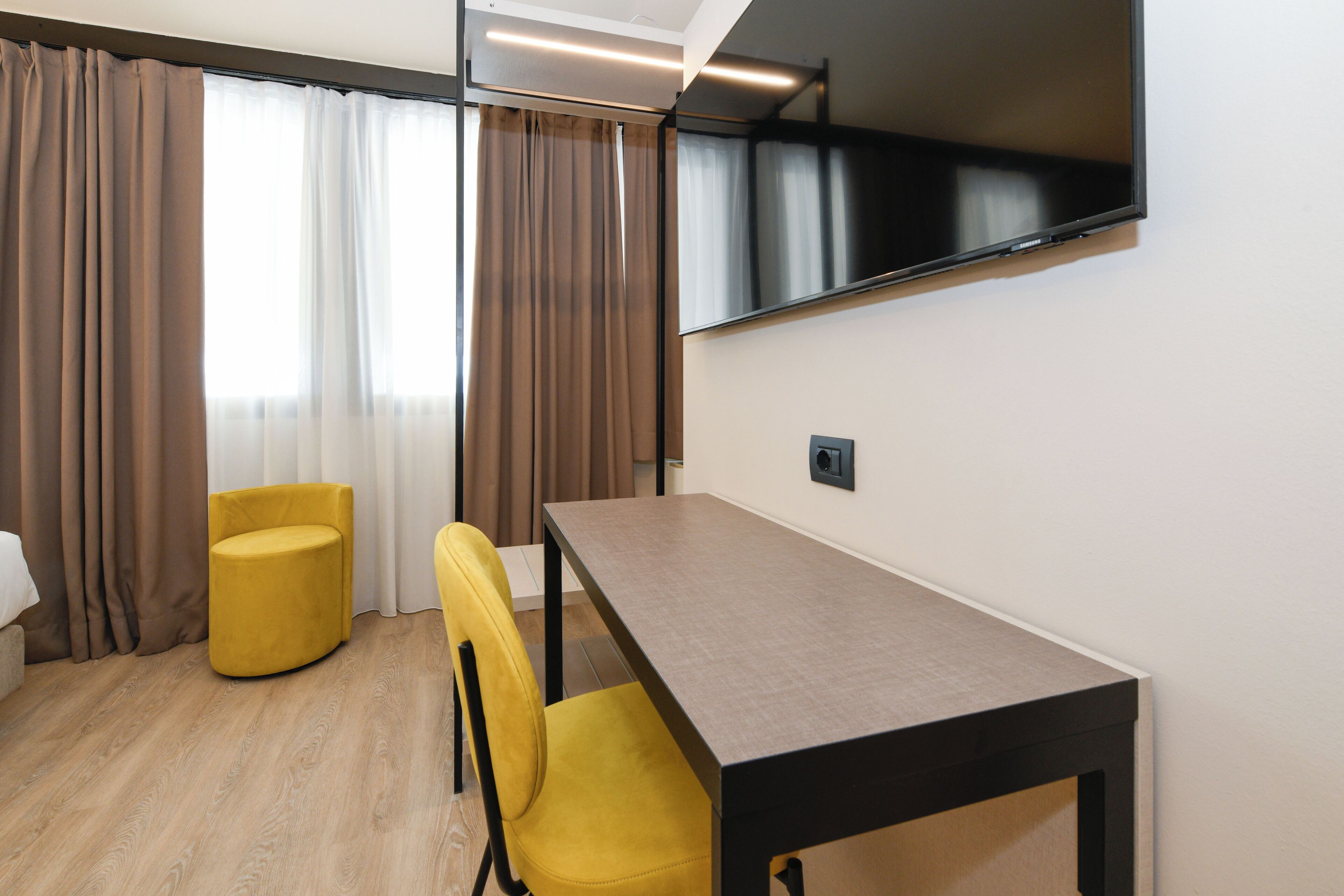 Ein modernes Hotelzimmer mit Holzboden, einem gelben Sessel, einem Tisch und einem an der Wand montierten Fernseher.
