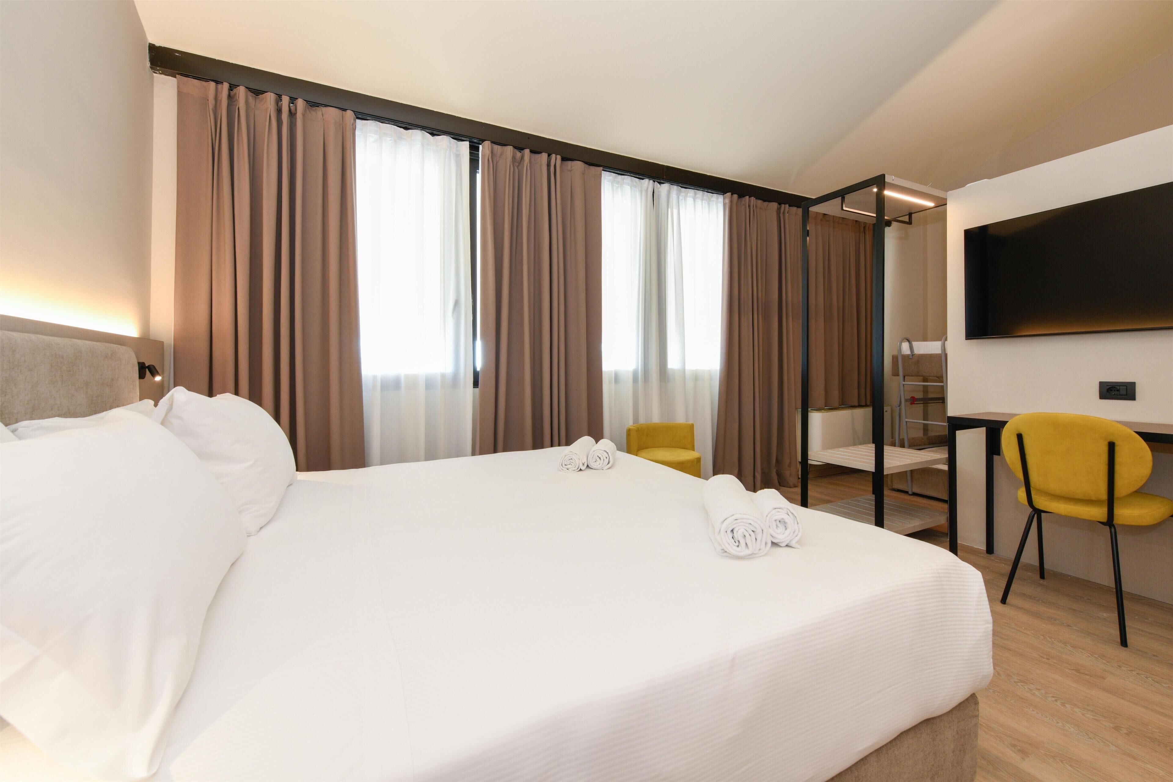 A hotel room with a large bed, two chairs, a desk, and a TV.