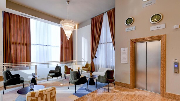 A hotel lobby with a chandelier, seating area, elevator, and clocks indicating different cities. - Best Western Hotel Garda (Affi)