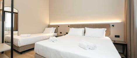 A hotel room with two single beds and one double bed, all neatly made with white linens and towels.