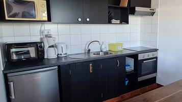 A compact kitchen with a microwave, toaster, kettle, sink, and a small refrigerator.