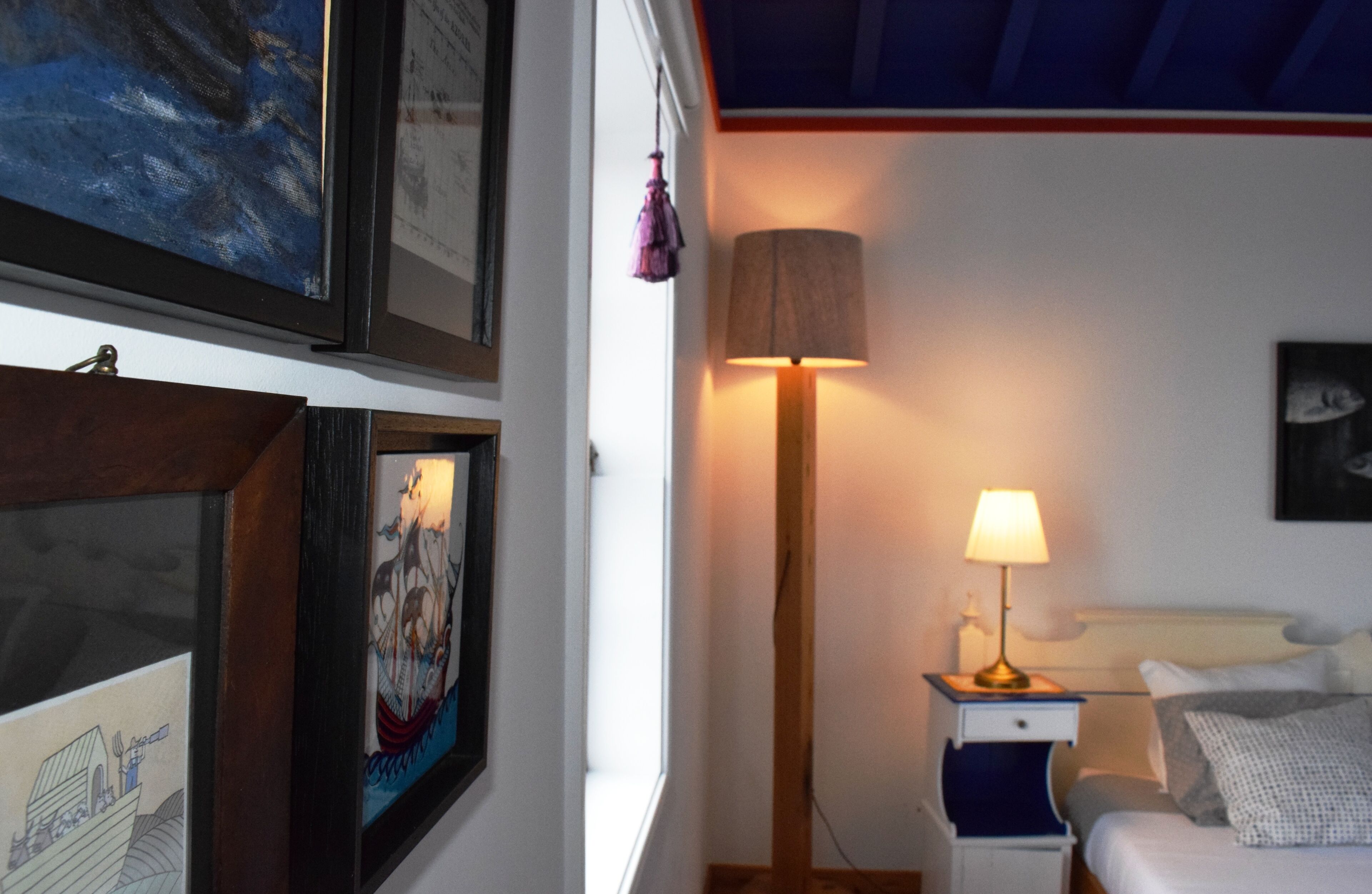 Un dormitorio con una cama, una mesita de noche con lámpara y cuadros en la pared.