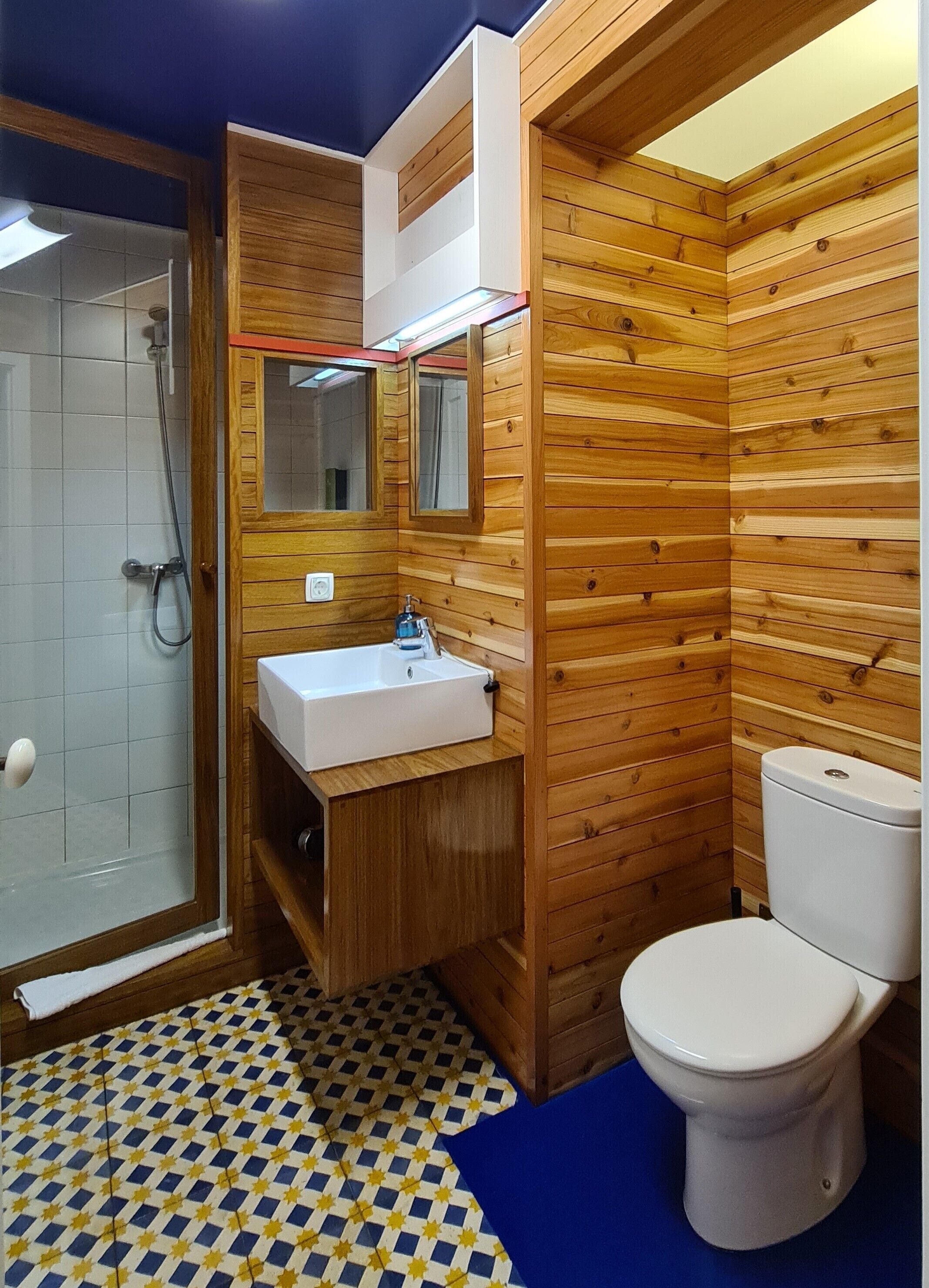 A bathroom with wooden paneling, a white sink, a mirror, and a toilet.