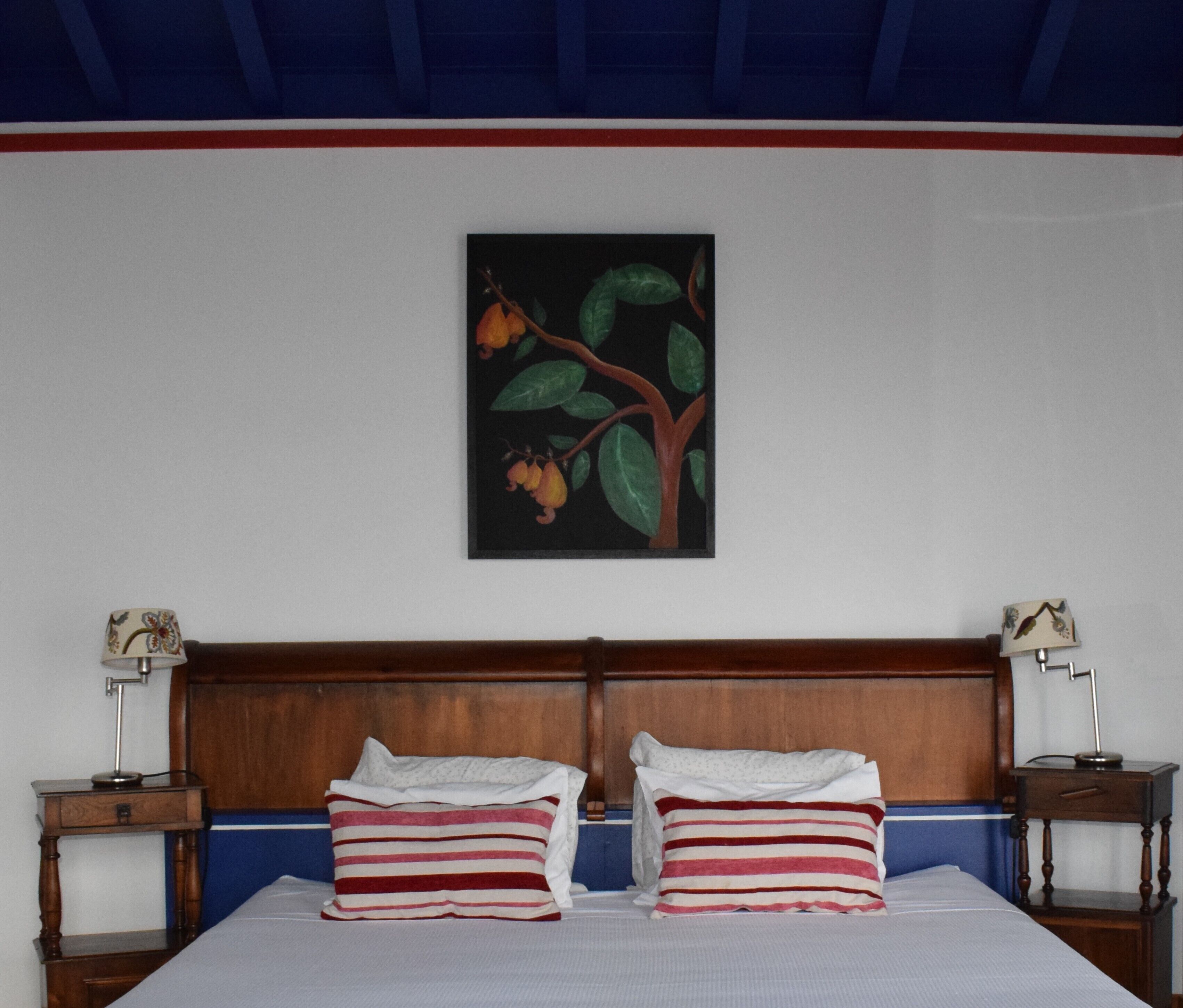Habitación de hotel con cama doble, dos mesitas de noche, cabecero de madera y un cuadro de una rama de árbol con hojas y frutos en la pared.