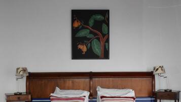 Habitación de hotel con cama doble, dos mesitas de noche, cabecero de madera y un cuadro de una rama de árbol con hojas y frutos en la pared.