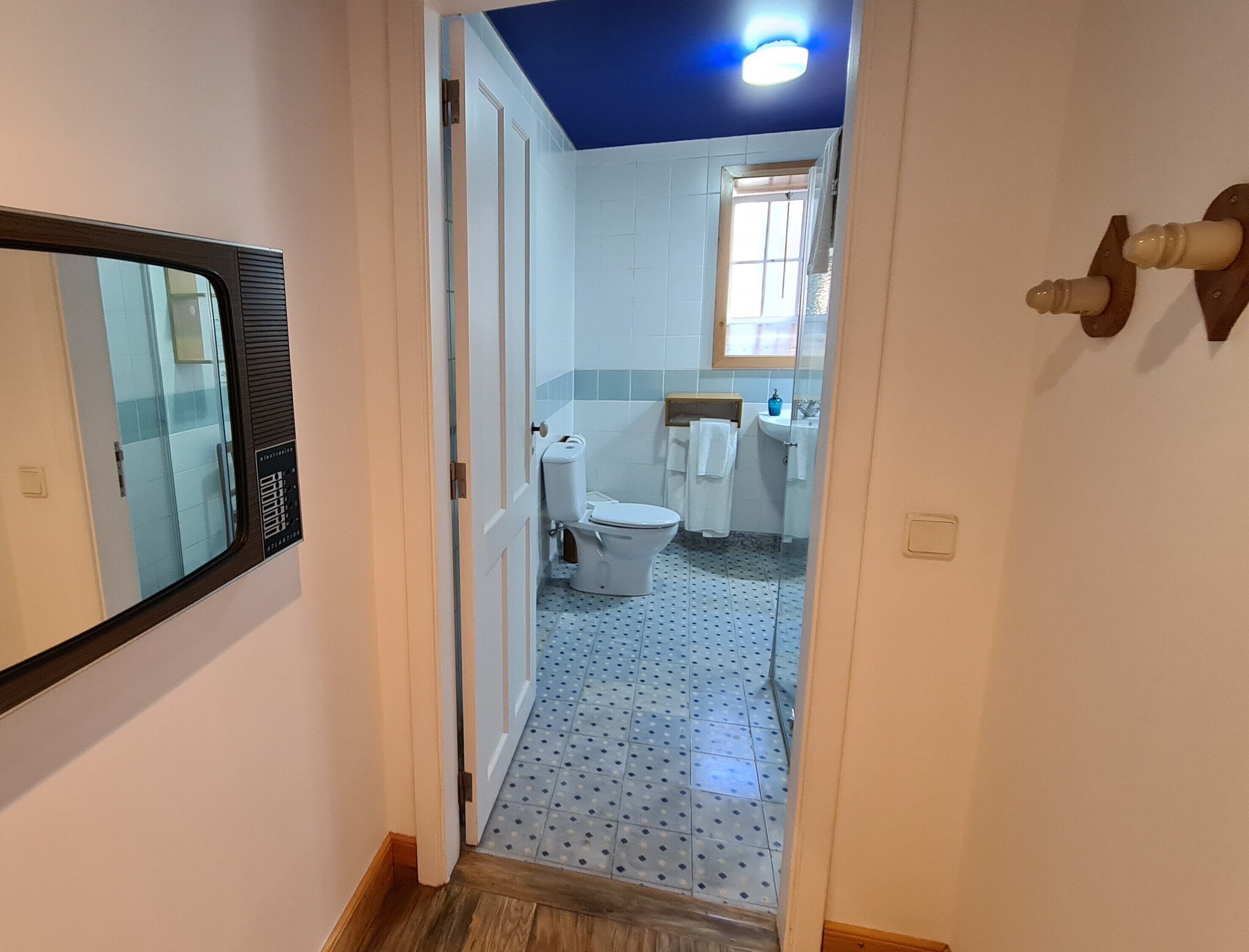 A narrow hallway leading to a bathroom with a toilet, sink, and window.