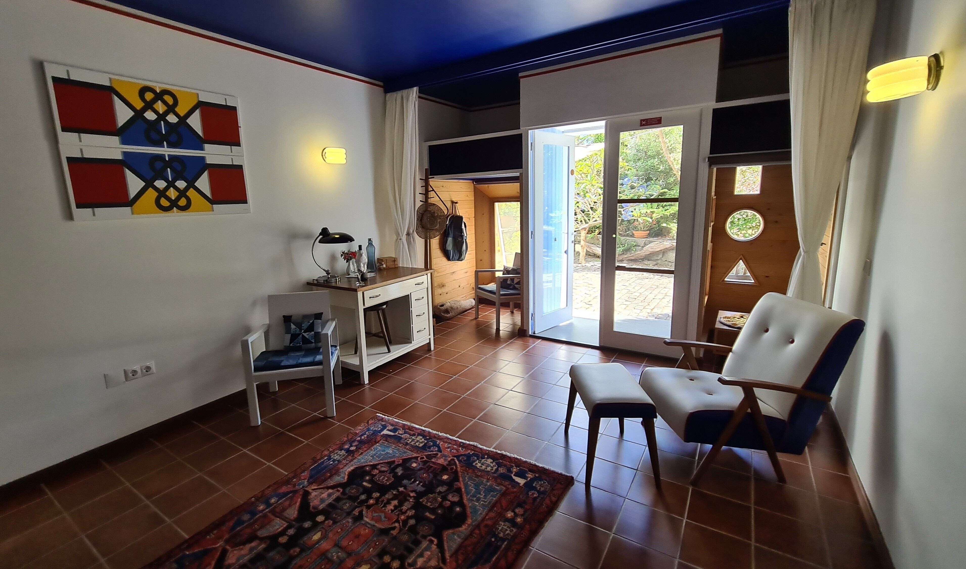 A room with a desk, chair, and a large rug. There is a sliding glass door leading to an outdoor area.