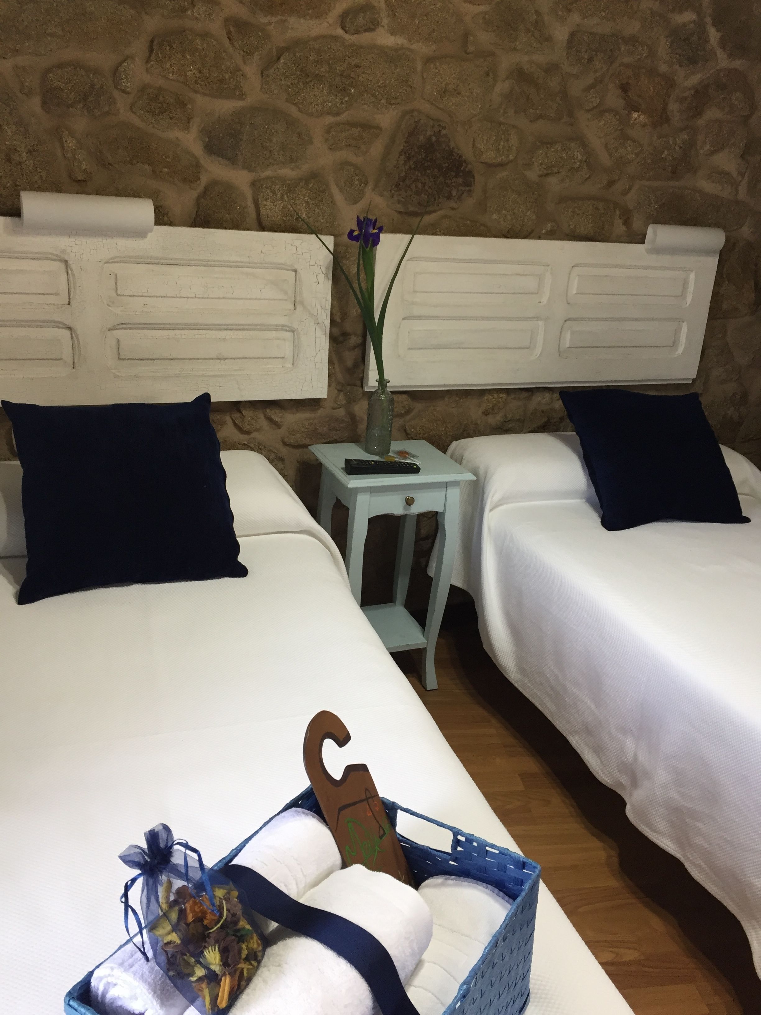 A room with two beds, a small table with a vase, and a basket with towels.