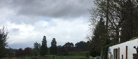 Un sendero de piedra conduce a un área de estar al aire libre con sillas y mesas, rodeado de follaje y un edificio blanco con ventanas.