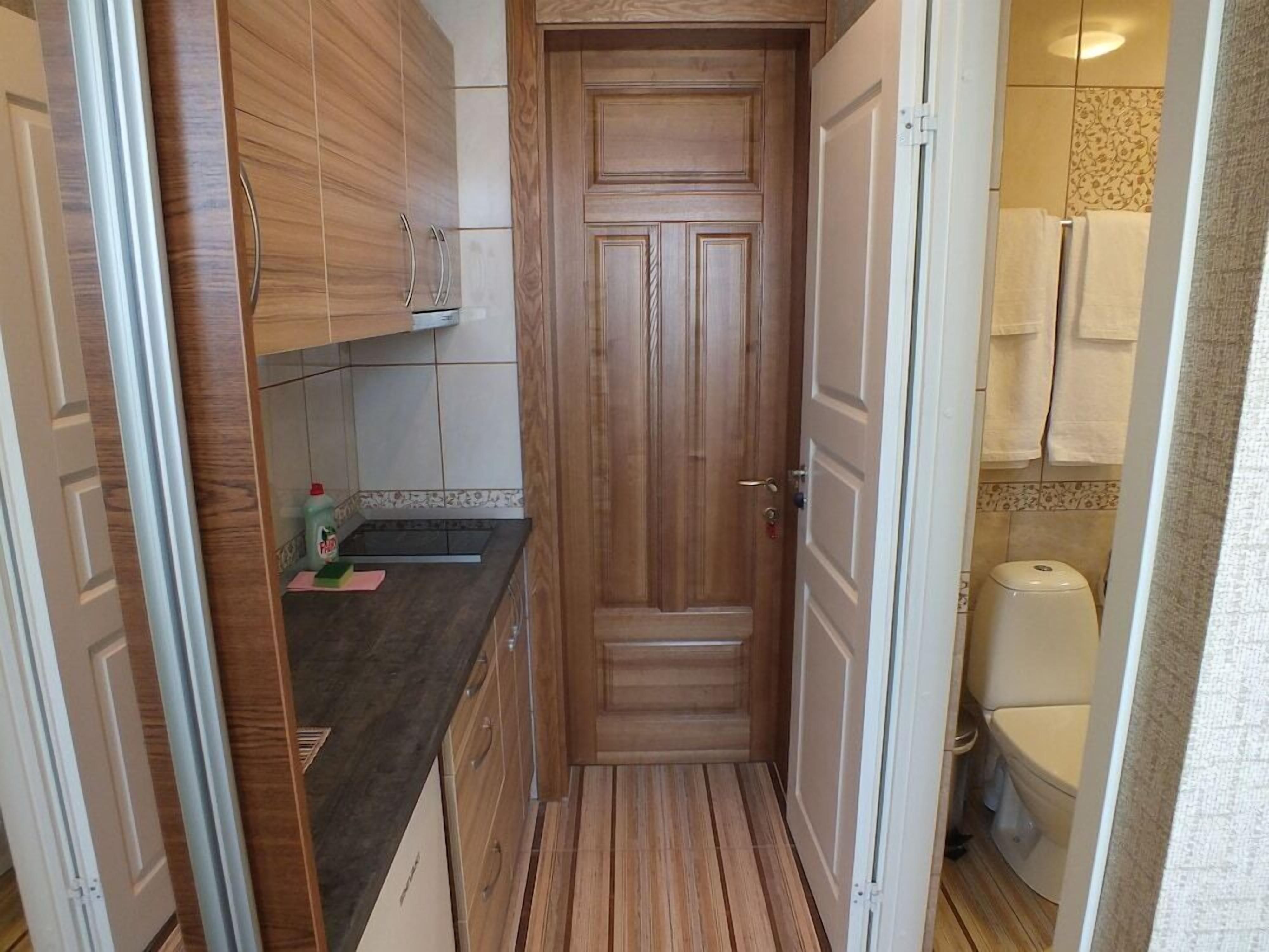 Eine schmale Küche mit Holzausstattung, einer schwarzen Arbeitsplatte und einer Tür zu einem Badezimmer mit Toilette und Handtuchhalter.