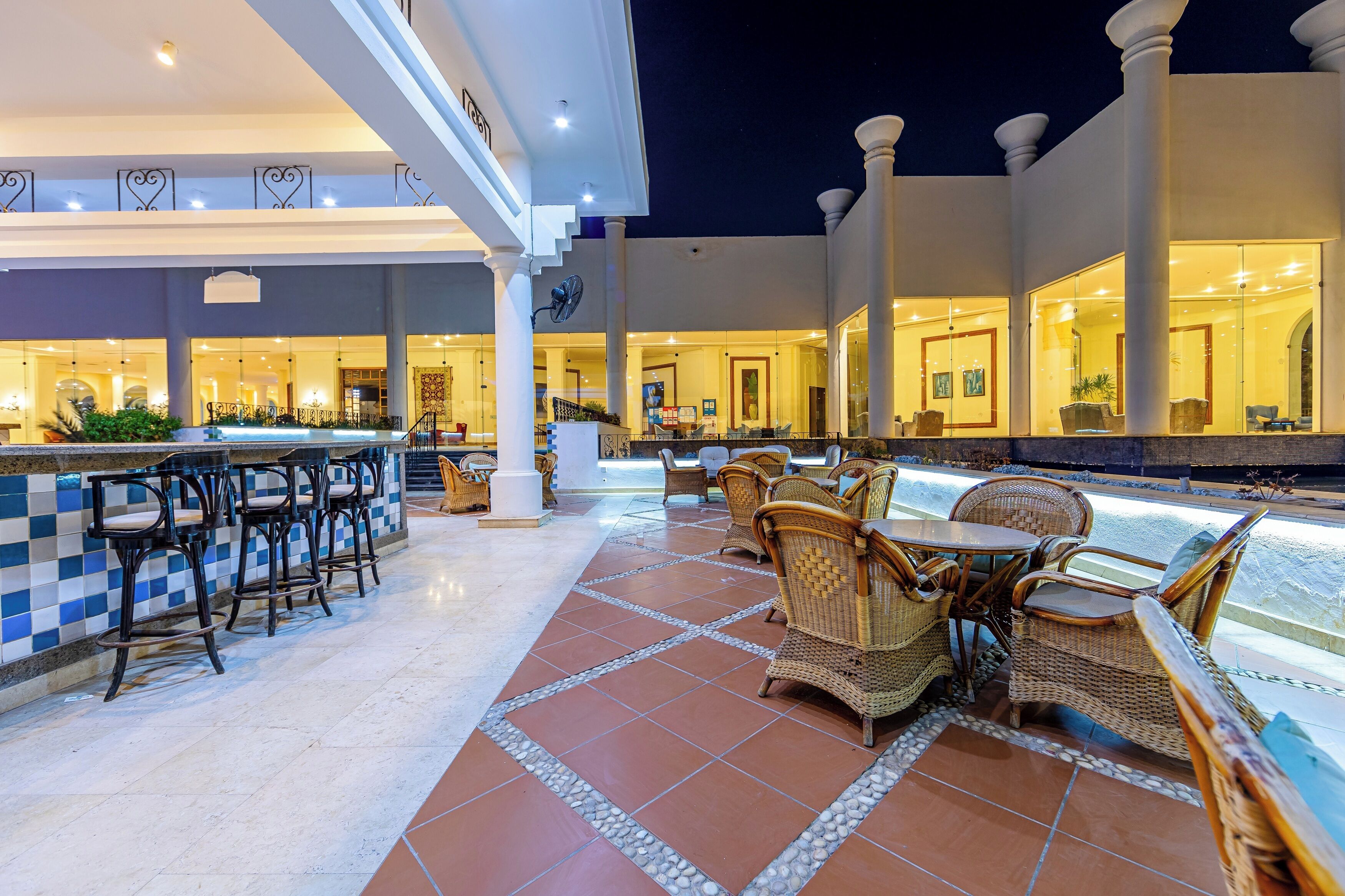 An outdoor seating area with bar stools and wicker furniture, a tiled floor, and a pool.