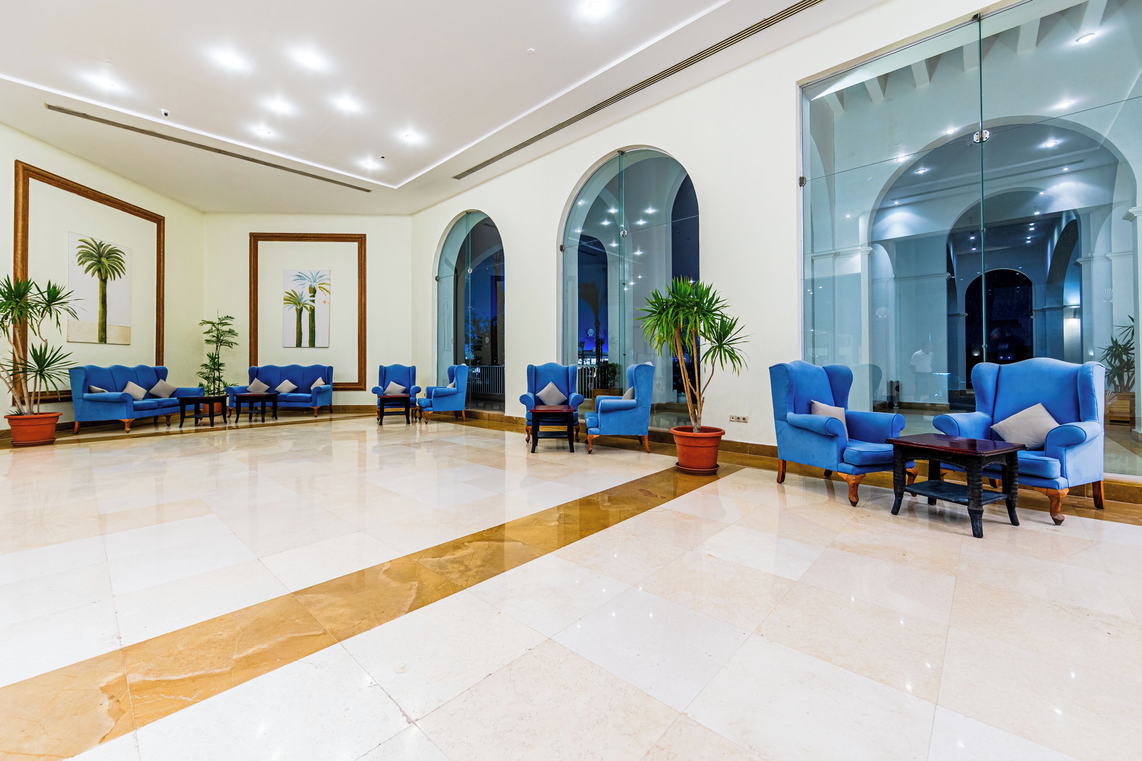 Un hall espacioso con sillones azules, una mesa de centro y grandes ventanales en arco.