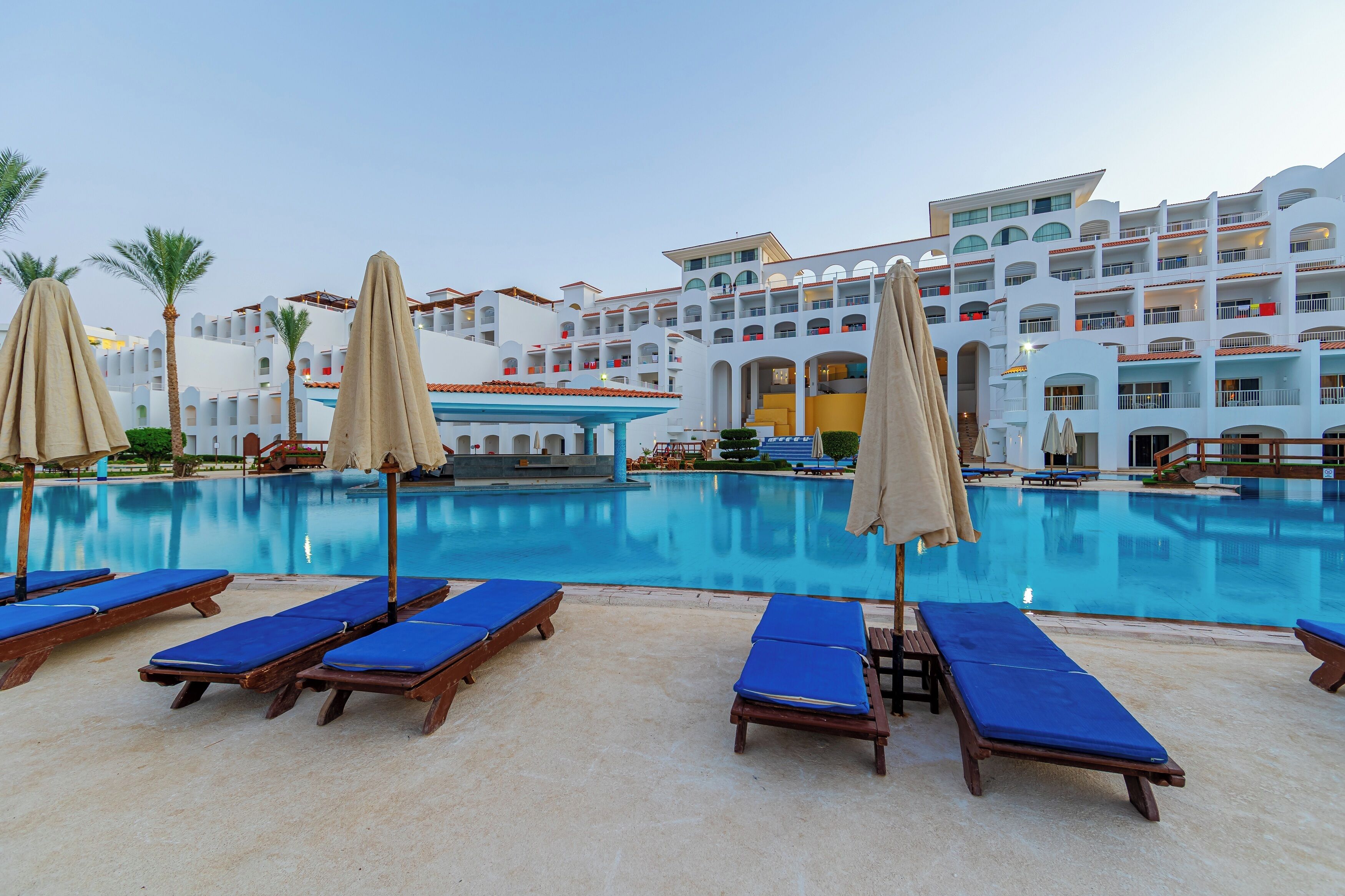 Un hotel con una piscina grande, tumbonas y sombrillas.
