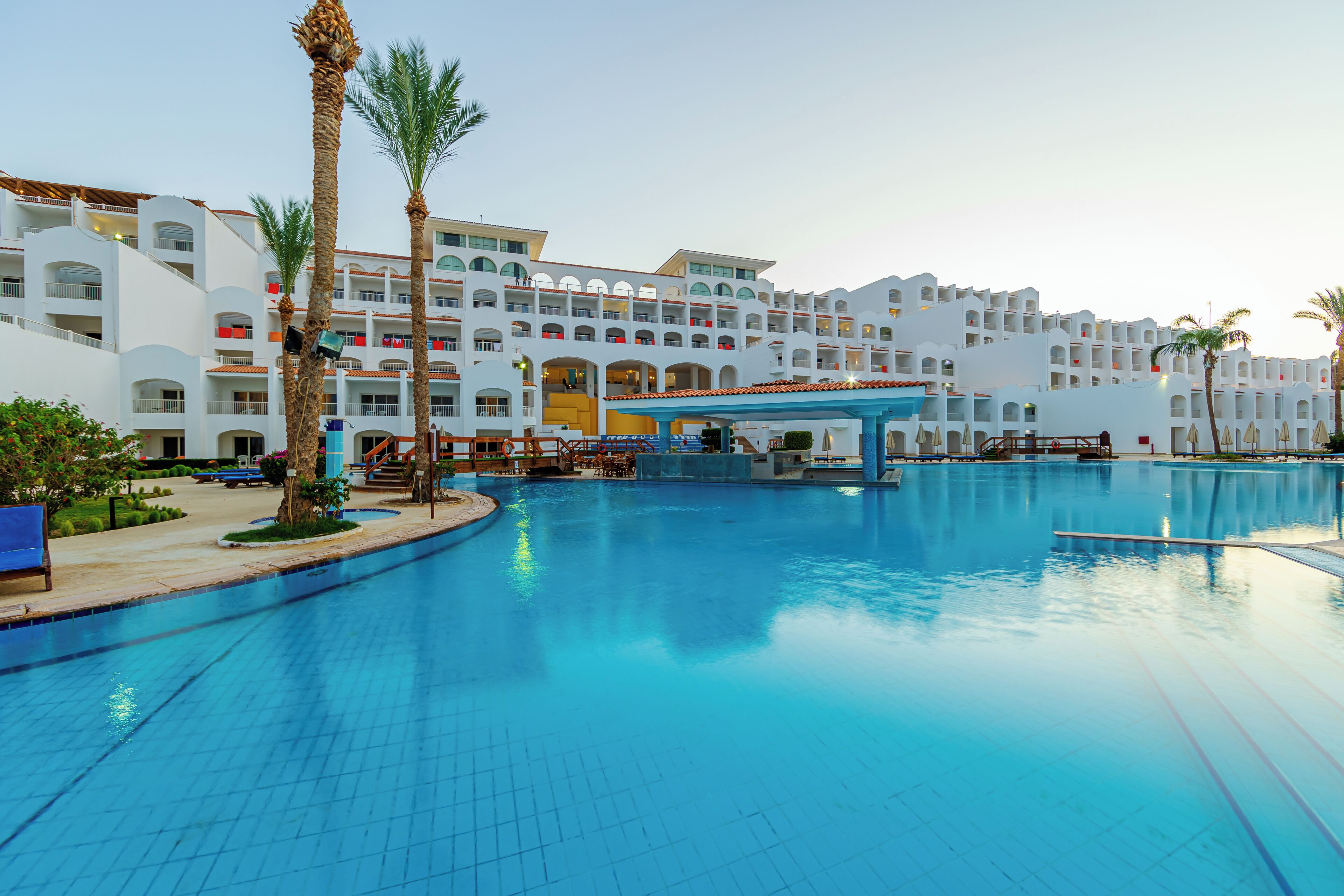 Un hôtel doté d’une grande piscine, de palmiers et d’un immeuble à plusieurs étages avec des balcons.