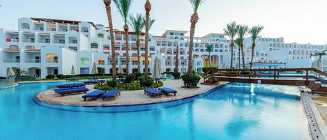 A swimming pool with lounge chairs, palm trees, and a hotel building with balconies.