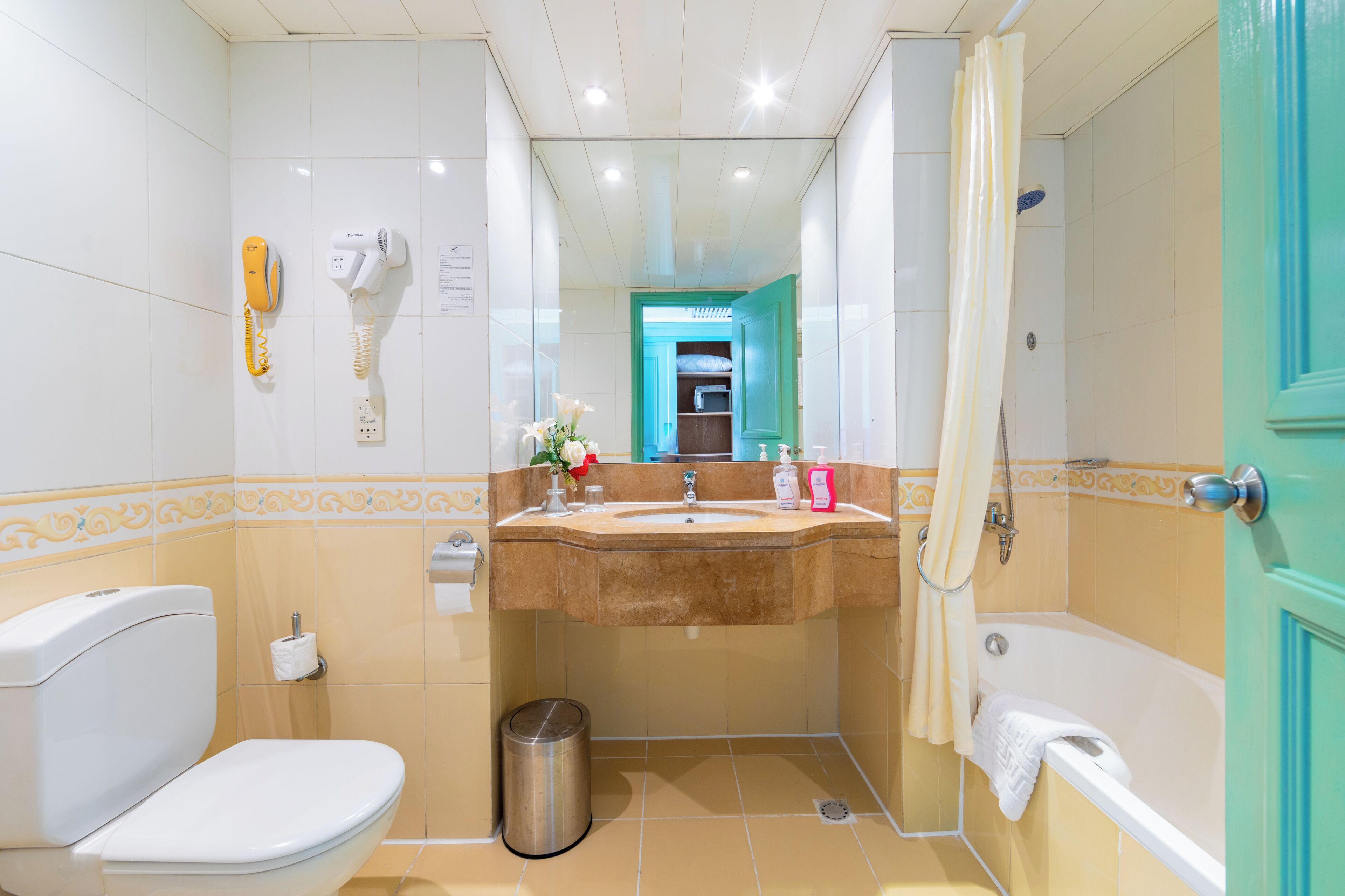 A bathroom with a toilet, sink, and bathtub, a mirror, and a trash can.